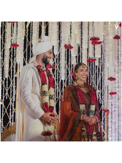 A candid moment of laughter between the bride and groom after the ceremony. The backdrop of cascading white and red florals adds a touch of classic elegance to their joyful interaction.