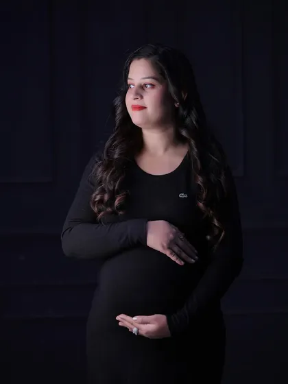 This dramatic portrait uses directional light to sculpt the subject's features and baby bump against a dark background, resulting in a classic and thoughtful image.