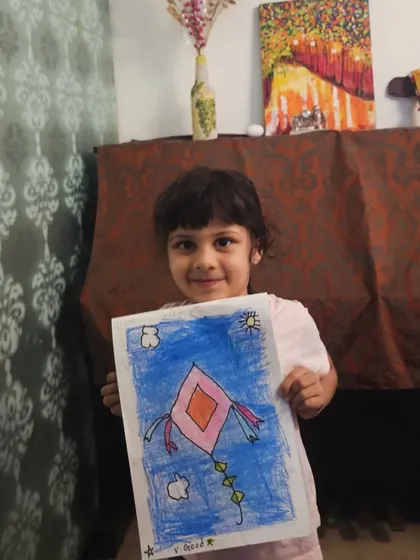 Look at that proud smile! A young student displays her colorful kite drawing, a perfect piece to celebrate the vibrant kite-flying season.