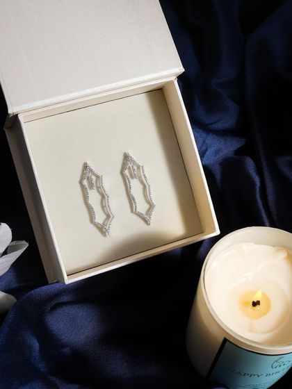 Creating a mood of quiet luxury. These uniquely shaped diamond earrings are presented in their box, accompanied by the soft glow of a candle, for an intimate and high-end feel.