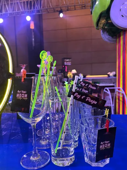 The details of a neon-themed party, showing custom stirrers and tags that carry the couple's name and event theme through to every glass.