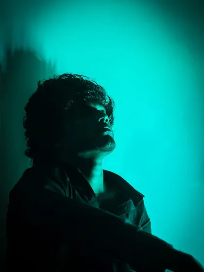 Another take on the silhouette, this time with the subject looking up into the light. The strong contrast between the dark figure and the bright teal background creates a feeling of drama and contemplation.