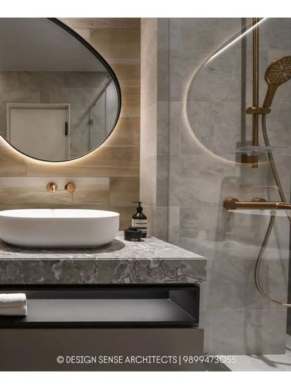 A modern bathroom combining a variety of textures. It features a stone-topped vanity with a vessel sink, a backlit oval mirror, and warm gold fixtures that add a touch of elegance.