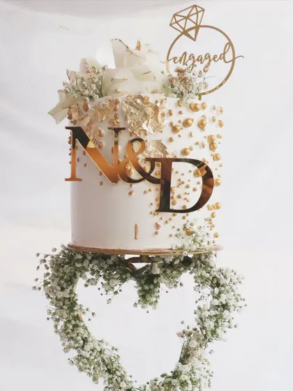 A detailed shot of the custom initial topper and gold leaf accents on this spectacular floating heart engagement cake.