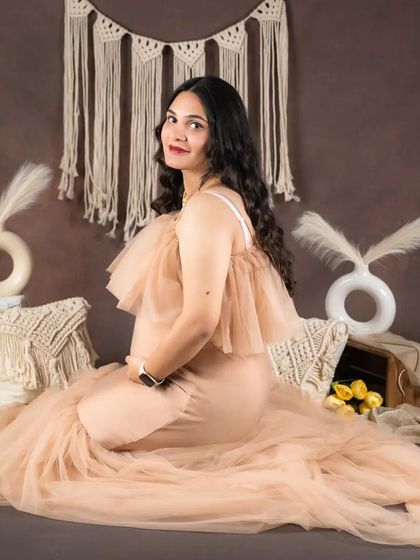 A gentle, seated pose from a boho maternity shoot. The setup includes macrame pillows, pampas grass, and soft lighting to create a comfortable and serene environment for your portraits.