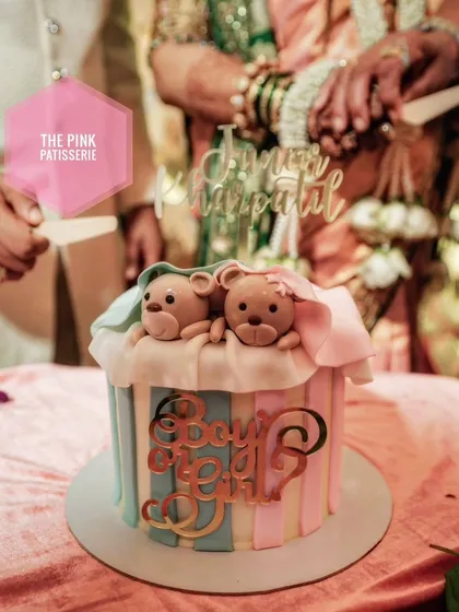 A "Boy or Girl?" gender reveal cake with pink and blue stripes and two adorable teddy bears under a blanket.