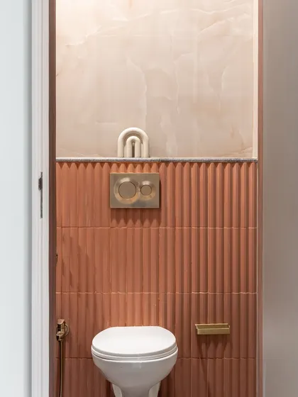 Texture takes center stage in this powder room. The fluted terracotta-colored tiles create a stunning feature wall, complemented by the soft, curved lines of the onyx-like panel above.
