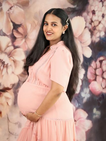 A stunning portrait of a mom-to-be against a beautiful floral backdrop. Her simple pink dress and happy smile make this a truly lovely and vibrant photo.
