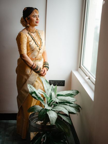 A full-length shot by the window, where natural light enhances the richness of her gold saree and the radiance of her makeup.