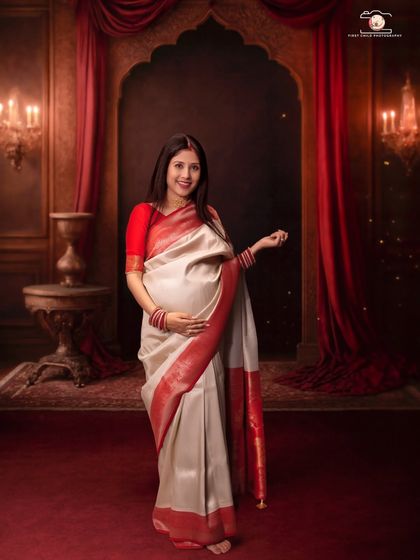A beautiful full-length portrait of the mother-to-be in a traditional saree. She stands gracefully in a regal studio setting, her hand gently resting on her baby bump, embodying strength and beauty.
