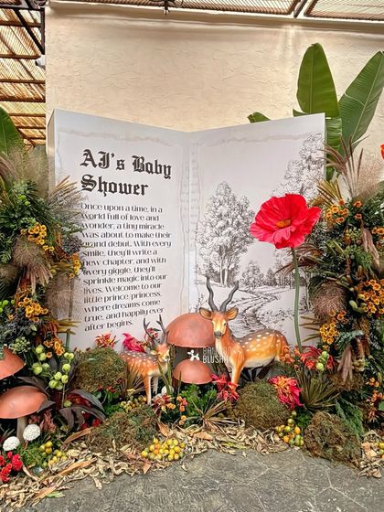 A storybook entrance for a woodland-themed baby shower, with a giant open book, mossy foliage, and cute deer figurines.