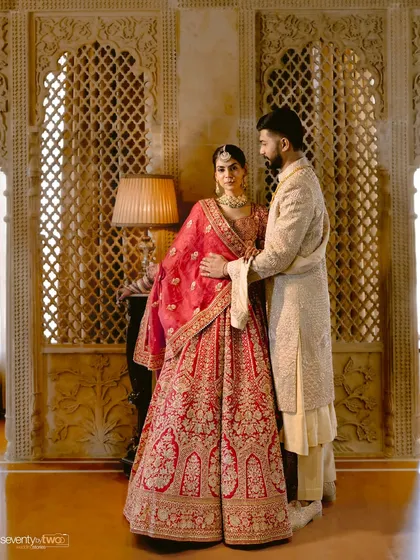 A regal portrait of the couple, their traditional red and cream outfits complementing the royal architecture of their wedding venue.