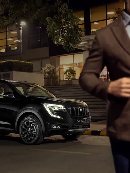 An outdoor lifestyle shot for the Mahindra XUV700. This image places the vehicle in a sophisticated urban environment, telling a story and connecting the product with the target audience's aspirations.