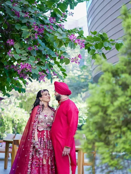 A romantic portrait of a Sikh couple at their Mehndi ceremony. The vibrant pink of their outfits stands out beautifully against the lush greenery.