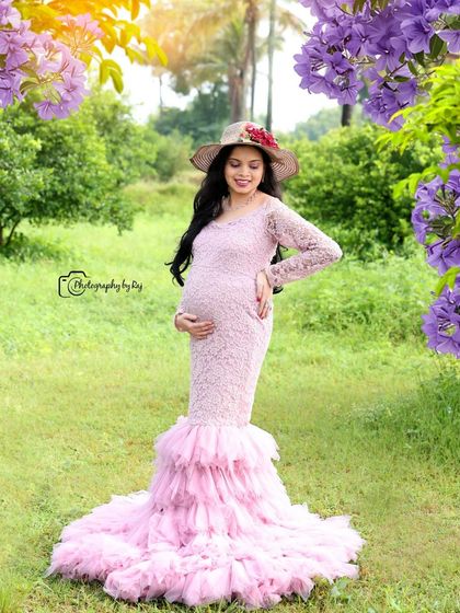 A beautiful solo portrait in a pink lace gown with a ruffled train. The mother-to-be is framed by purple flowers, creating a soft and romantic image.