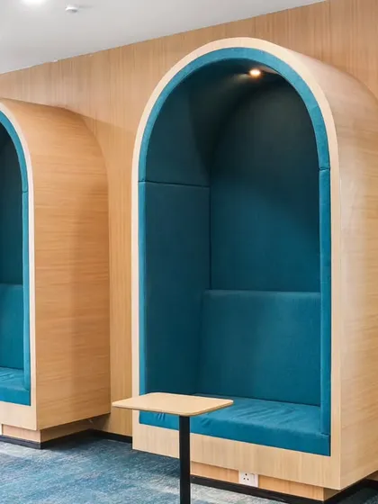 Modern acoustic phone booths in the office, providing private spaces for calls and focused work. The curved design and bold teal upholstery add a stylish and functional element to the open-plan workspace.