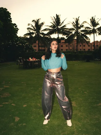 A dreamy, outdoor editorial shot with Dhvani Bhanushali. The custom candy blue top and metallic pink Ganni pants create a beautiful contrast against the green lawn at dusk.