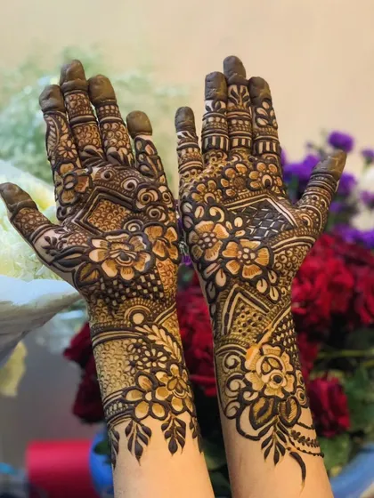 The palms are decorated with a mix of floral motifs and geometric patterns, held up against a backdrop of flowers.