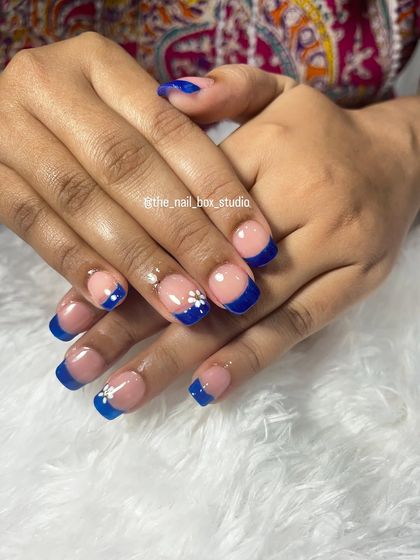 This photo shows the full set of the royal blue French tip nails. The pop of color is fun and unexpected, while the flower adds a touch of femininity.