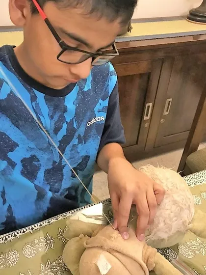 With focused concentration, a young boy stitches up his favorite toy. This activity not only teaches a practical skill but also fosters a sense of responsibility and care for one's belongings.