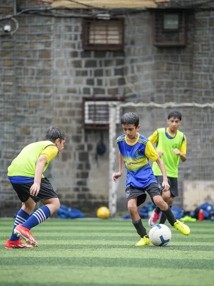 A young player in our blue and yellow kit skillfully maneuvers the ball around a defender. This image emphasizes that while talent gets you on the pitch, consistent effort is what keeps you in the game.