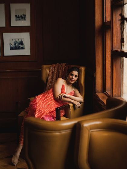 A beautiful portrait of Isha Talwar seated in a leather armchair. The rich, dark tones of the room create a warm and intimate atmosphere.