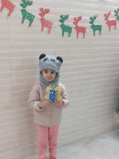 Dressed warmly for a winter session, this child shows off her butterfly craft against a festive Christmas background. We celebrate all seasons with creative activities.