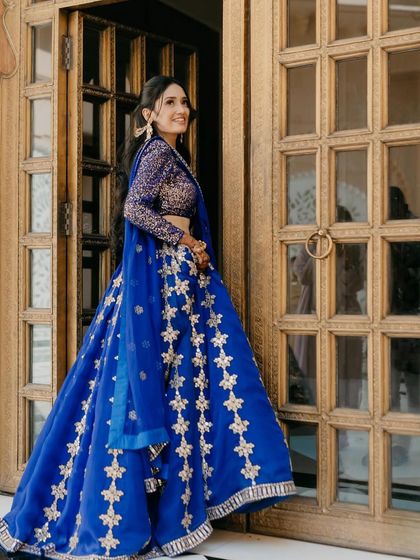 A vibrant bridal portrait in a royal blue lehenga. The bride's happy expression as she peeks out from a golden doorway at The Oberoi Udaivilas creates a joyful and regal image.