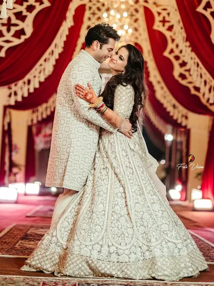 A sweet, candid moment as the groom kisses the bride's cheek, their coordinated white outfits creating a look of pure elegance.