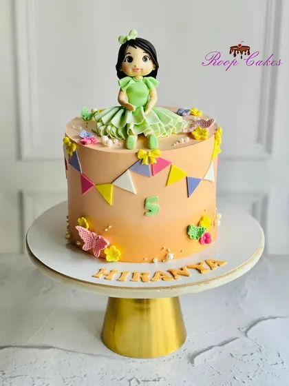 The cutest cake for the cutest 5-year-old. This design features a sweet doll topper, colorful bunting, and a soft peach ombre effect.