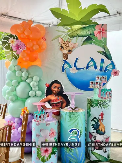 This Moana party decor features themed plinths and a tropical balloon garland. The setup is perfect for a cake and dessert table.