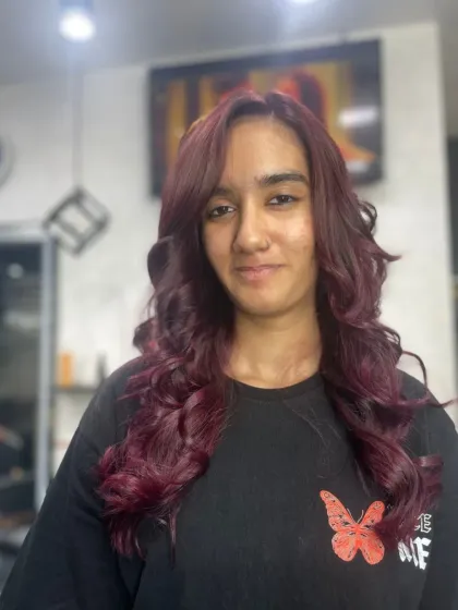 A happy client showing off her new look, featuring a beautiful deep red color styled into soft, romantic curls.