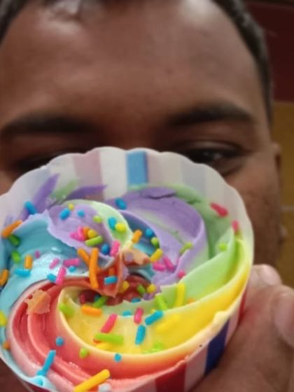 One of our customers holding up a rainbow cupcake. The bright colors and cheerful sprinkles bring a smile to everyone's face.