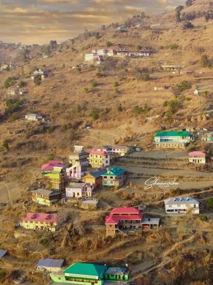 A wide shot of the colorful village houses built on the hillside in Dharech. This image captures the vibrant character and unique setting of a traditional Himachali settlement.
