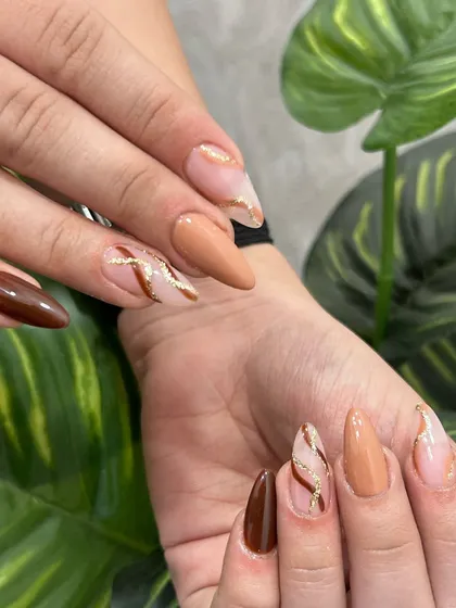 Earthy tones with a touch of glam. This set of almond-shaped extensions features a mix of solid brown, nude, and a beautiful marble design with gold glitter accents.