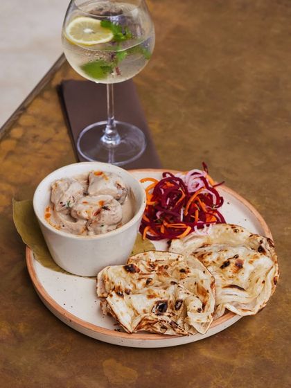 A plate of our creamy chicken malai with soft, layered naan and a side of pickled onions, paired with a refreshing gin and tonic. A simple, yet perfect, pairing.