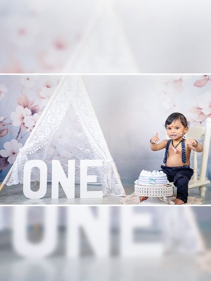 A simple and elegant first birthday moment. The focus is on the happy baby and his cake, set against a soft and dreamy floral backdrop.
