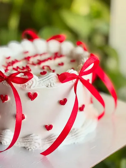 A side view of the "Will you be my Valentine?" cake, highlighting the tiny red hearts on the side and the playful red bows.