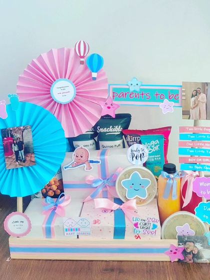 This hamper is all about celebrating the parents-to-be. It includes snacks, personalized photo frames, and gift boxes, all tied together with a pink and blue star theme.