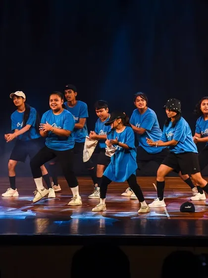 The hip-hop team executes a powerful, synchronized move. Dressed in matching blue shirts and streetwear, they embody the cool, urban energy of the dance style.