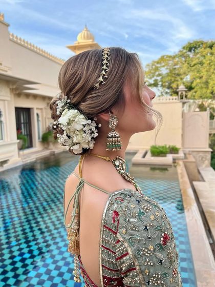 A side profile of a romantic floral updo, showing how the flowers and a delicate hair chain are placed to complement the bride's jewelry.