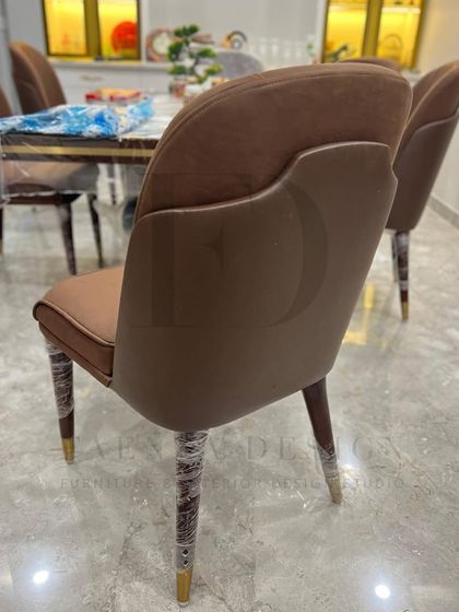 A close-up of one of my favorite dining chair designs. It features a two-tone upholstery in a rich brown, with elegant curves and tapered legs capped in brass, embodying understated luxury.