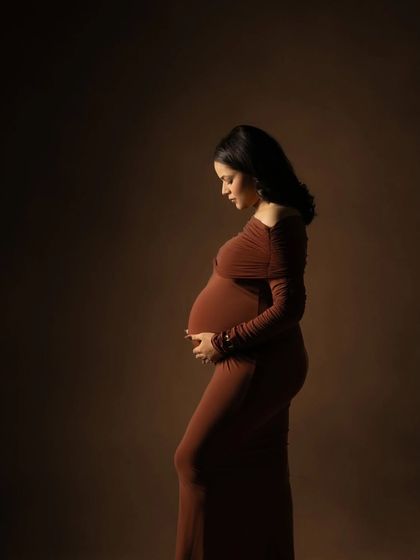 A classic silhouette portrait. The mother-to-be is captured in profile against a dark background, with soft light sculpting the beautiful curve of her baby bump.