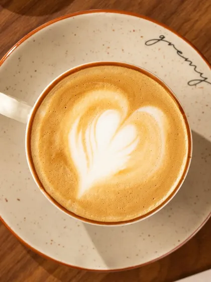 A beautifully made cappuccino with latte art, served on a plate with the cafe's logo.