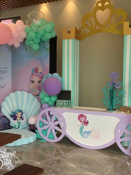 A wider view of the indoor mermaid party setup, showing the storybook backdrop and the themed carriage.