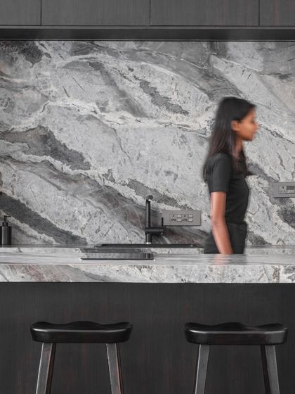 The open kitchen and bar area features a striking grey granite backsplash and countertop. It's a functional space designed for both everyday living and entertaining, continuing the home's monochrome theme.