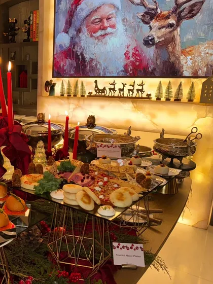 The full Christmas dinner spread, with a grazing platter, hot food in chafing dishes, and a Santa Claus painting in the background.