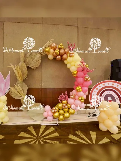 A chic, boho-style photo ring for the Annaprashan ceremony. The ring is decorated with pastel pink and yellow balloons, dried palm leaves, and accented with a butterfly and rainbow prop.