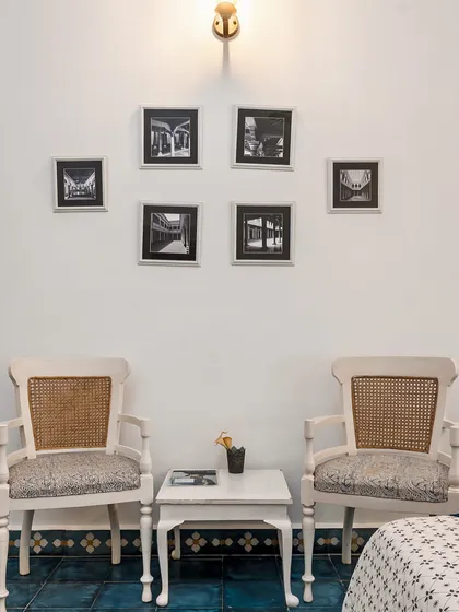 A cozy seating arrangement with classic, colonial-style chairs and a gallery wall of black and white architectural photos. The decor is timeless, elegant, and tells a story of place and history.