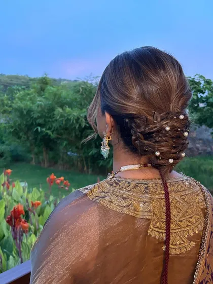 A detailed view of the braided and twisted low bun, dotted with pearls. The intricate details make this a truly special hairstyle.